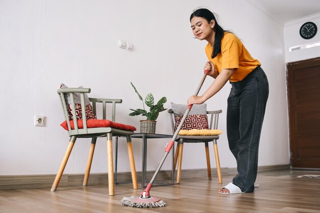 Junge asiatische Frau wischt Boden im Wohnzimmer