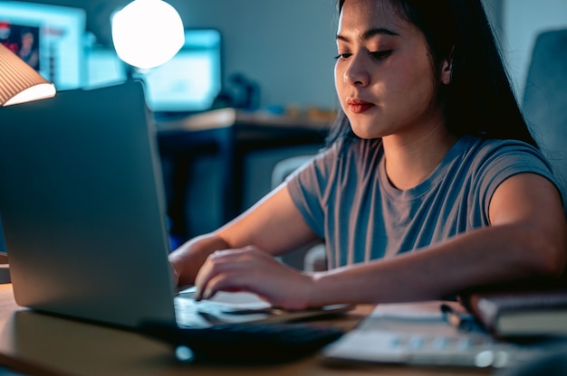 Junge asiatische Frauen arbeiten mit Laptop im Wohnzimmer zu Hause im Dunkeln an der LampeArbeiten von zu Hause aus