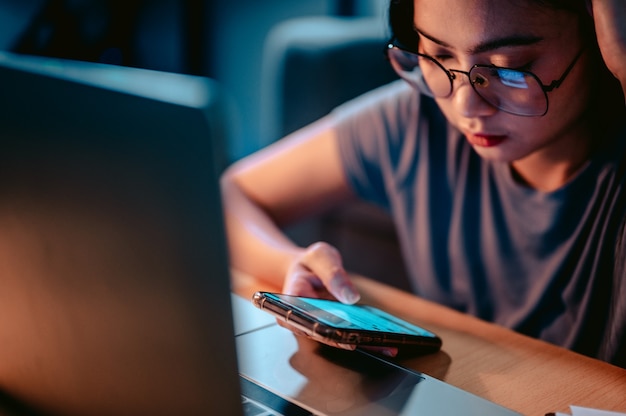 Junge asiatische Frauen arbeiten mit Laptop im Wohnzimmer zu Hause im Dunkeln an der LampeArbeiten von zu Hause aus