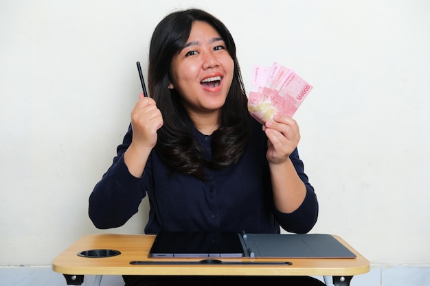 Junge asiatische Frauen lächeln glücklich, wenn sie Papiergeld mit Handy-Tablet auf dem Tisch halten