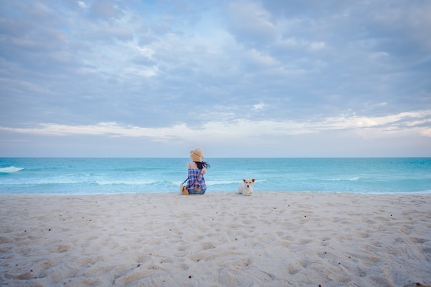 junge asiatische Frauen sitzen traurig am Strand am Meer mit einem Hund, sitzen am Strand im Hintergrund