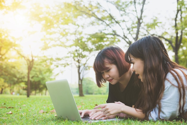 Junge asiatische Frauenbeine auf dem grünen Gras mit offenem Laptop