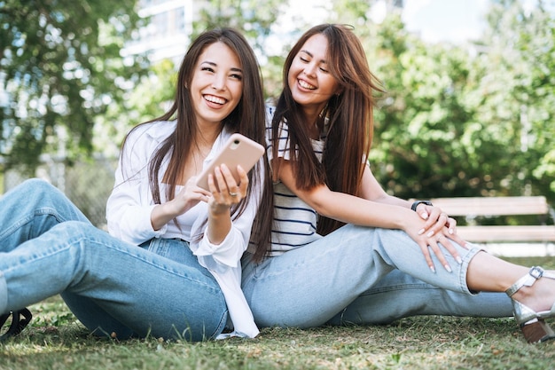 Junge asiatische Freundinnen mit Handy haben Spaß im Stadtpark
