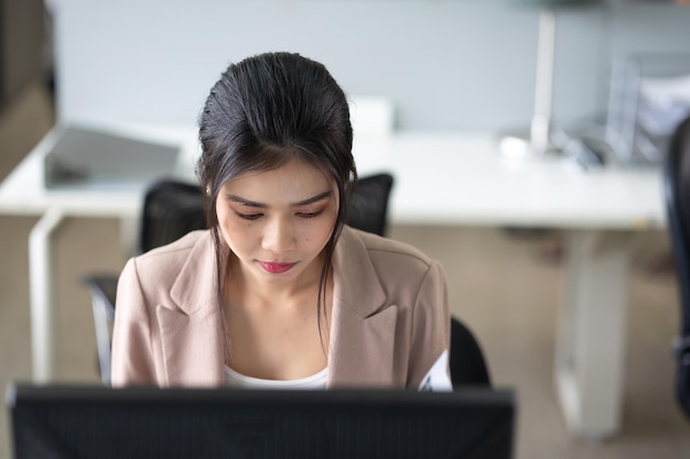 Junge asiatische Geschäftsfrau, die am Schreibtisch mit Desktop-Computer im modernen Heimbüro arbeitet