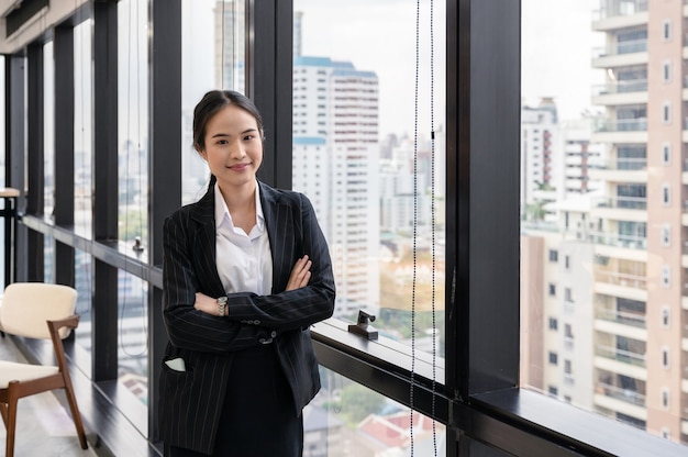 Junge asiatische Geschäftsfrau, die gekreuzten Arm im Büro steht