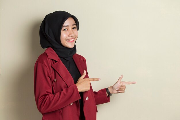 Junge asiatische Geschäftsfrau, die Hijab trägt, der zuversichtlich zeigt, mit den Fingern in verschiedene Richtungen zeigend.