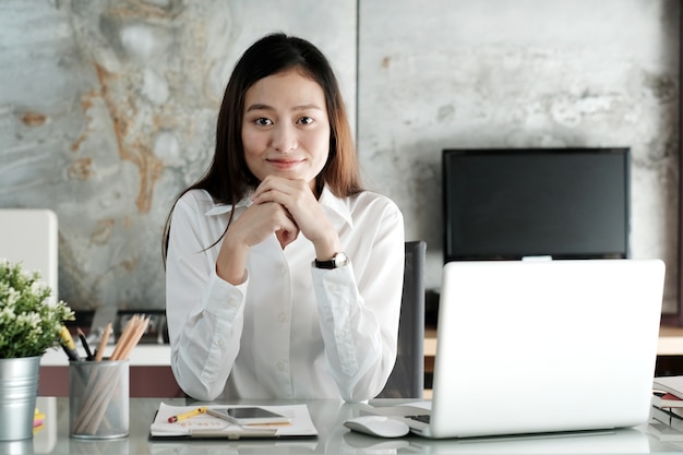 Junge asiatische Geschäftsfrau, die mit mit lächelndem Gesicht am Schreibtisch arbeitet