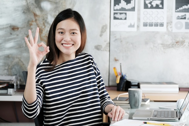 Junge asiatische Geschäftsfrau, die okayhandzeichen zeigt