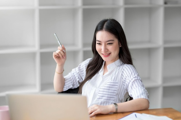 Junge asiatische Geschäftsfrau freut sich, im modernen Büro mit einem Laptop-Computer zu arbeiten.