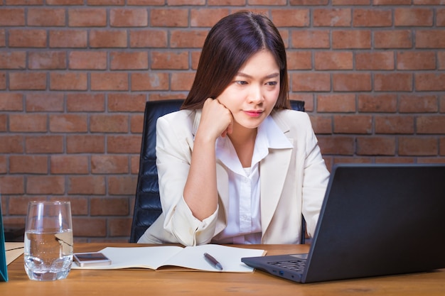 Junge asiatische Geschäftsfrau in der Klage, die spät an ihrer Laptop-Computer in ihrem Büro arbeitet
