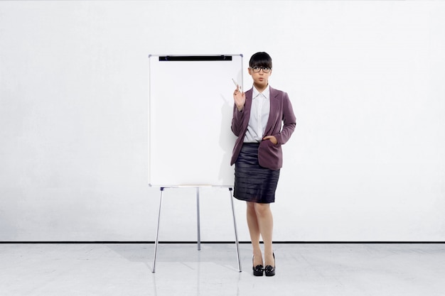 Junge asiatische Geschäftsfrau mit dem Markierungsstift, der neben whiteboard steht