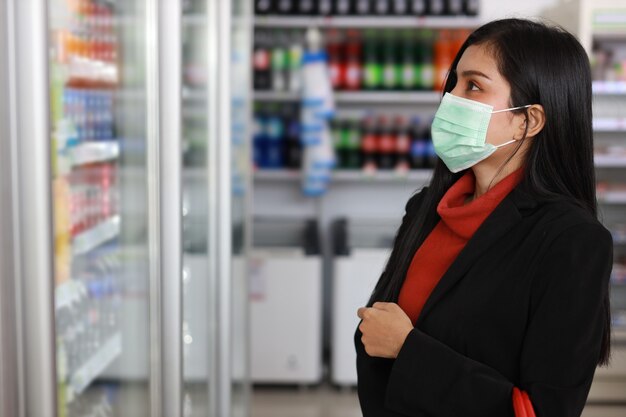 Junge asiatische Geschäftsfrau mit Gesichtsmaske, die Lebensmittel sucht und auswählt, um sie im Regal im Supermarkt-Kaufhaus oder Einkaufszentrum zu kaufen?