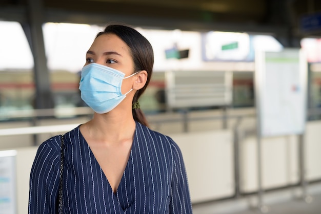 Junge asiatische Geschäftsfrau mit Maske, die an der Skytrainstation wartet