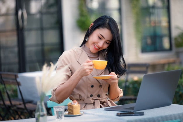 Junge asiatische Geschäftsfrauen und freiberuflich sitzend auf Holztisch im Garten und entspannendem Kaffeetrinken