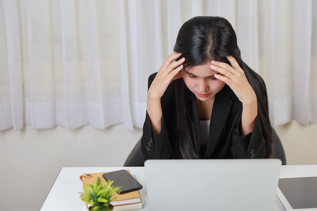 Junge asiatische gestresste Geschäftsfrau, die Probleme hat oder Schmerzen an den Schläfen hat, leidet unter Kopfschmerzen oder Migräne, nachdem sie zu lange am Computer gearbeitet hat. Office-Syndrom-Konzept