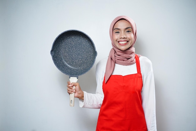 Junge asiatische Hausfrau mit Küchenschürze, die eine Pfanne kocht und hält