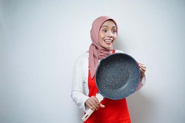 Junge asiatische Hausfrau mit Küchenschürze, die eine Pfanne kocht und hält