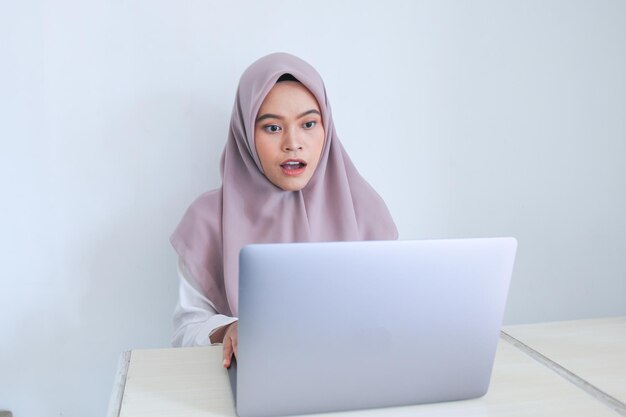 Junge asiatische Islamfrau mit Kopftuch ist ernster Blick auf den Laptop Indonesische Frau auf grauem Hintergrund