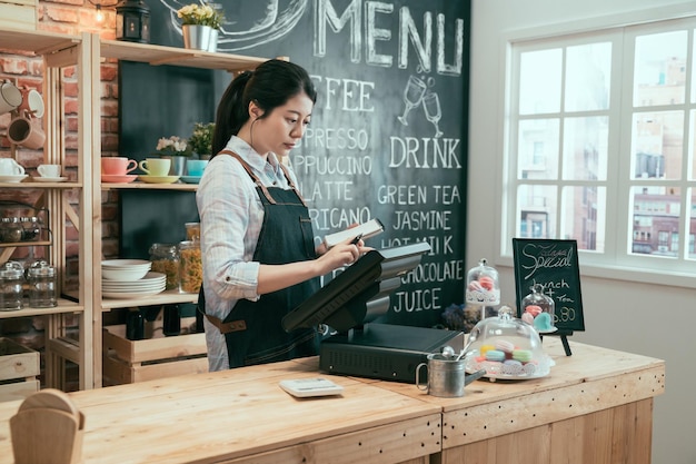 Junge asiatische japanische Kellnerin, die ein digitales Gerät für die Zahlung an der Theke des Cafés verwendet. schöne frau mitarbeiter geben kundenbestellung von notiz in verkaufsterminalmaschine im cafégeschäft ein.