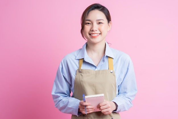 Junge asiatische Kellnerin, die auf rosa Hintergrund steht