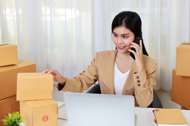 Junge asiatische kluge und glückliche Geschäftsfrau im lässigen Kleid, das von zu Hause mit Laptop-Computer und Smartphone arbeitet