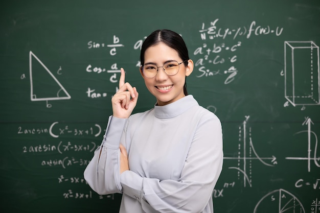 Junge asiatische Lehrerin, die im Stehen den Zeigefinger und eine Videokonferenz mit der Schülerkamera unterrichtet Lehrerin trainiert die Mathematik in der Klassenzimmertafel aus dem Online-Kurs