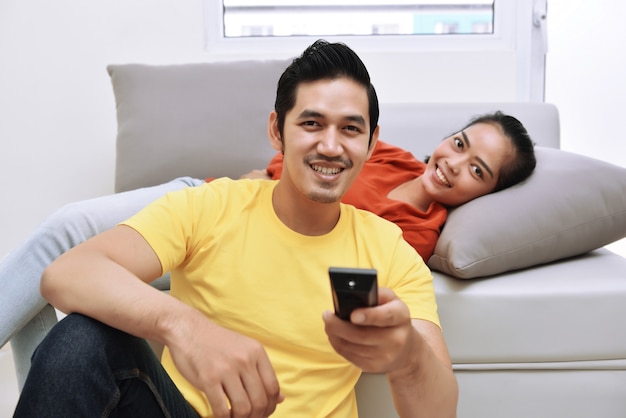 Junge asiatische liebevolle Paare, die fernsehen und sich entspannen