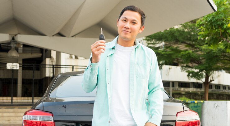 Junge asiatische Mannhand, die seinen Schlüssel im Auto hält. Konzept des Mietwagens oder des Autokaufs.