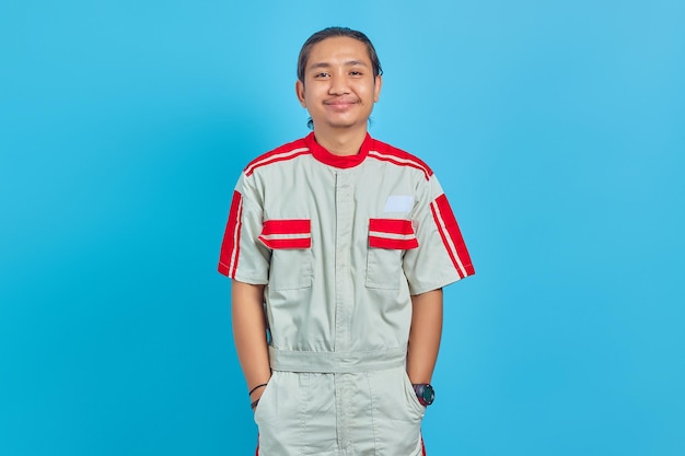 Junge asiatische Mechaniker in Uniform lächelnd in die Kamera schaut auf blauem Hintergrund