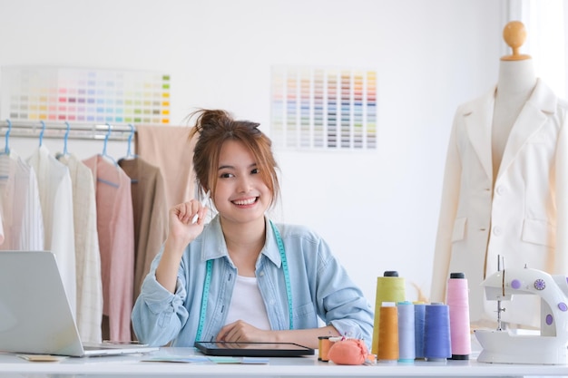 Junge asiatische Modedesignerin sitzt an ihrem Schreibtisch im Designstudio