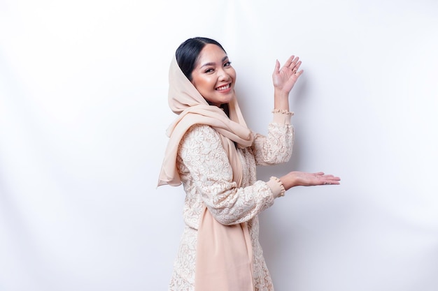 Junge asiatische muslimische Frau, die lächelt, während sie zeigt, um Platz neben ihr zu kopieren