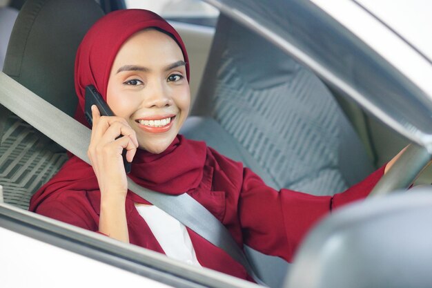 Junge asiatische muslimische Frau im Hijab benutzt Smartphone und lächelt im Auto