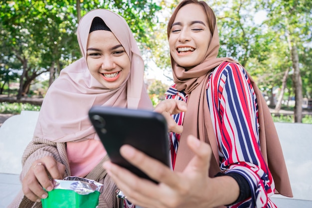 Junge asiatische muslimische Frau im Kopftuch treffen Freunde und Telefon im Park