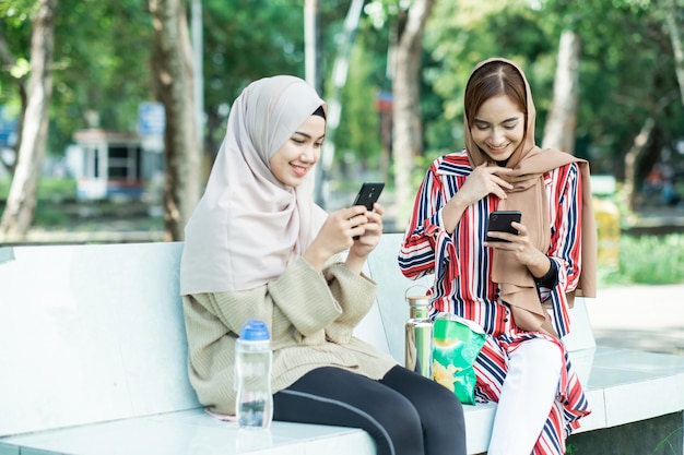 Junge asiatische muslimische Frau im Kopftuch treffen Freunde und Telefon im Park