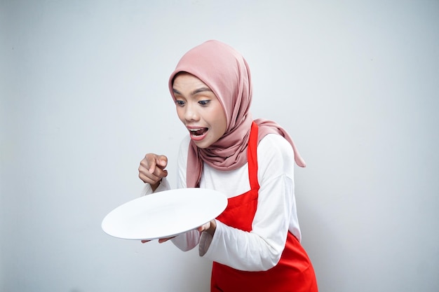 Junge asiatische muslimische Frau in Schürze steht und hält leere weiße Platte