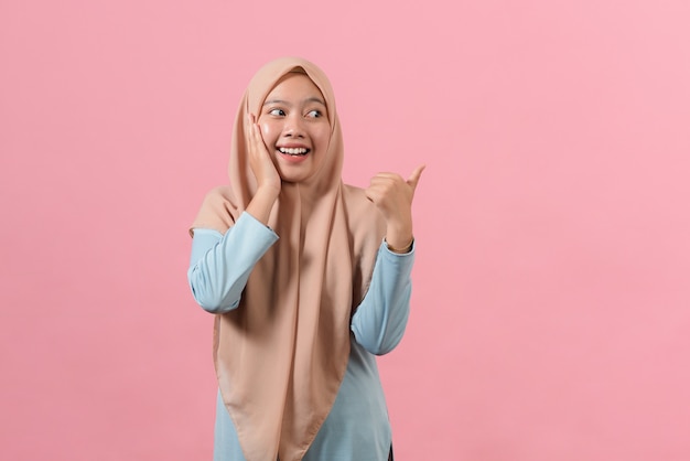 Junge asiatische muslimische Frau lächelnde Punkte beiseite auf Kopienraum zeigt, dass Werbung muslimische Freizeitkleidung trägt