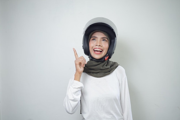 Junge asiatische muslimische Frau lächelt und denkt mit Motorradhelm isoliert auf weißem Hintergrund