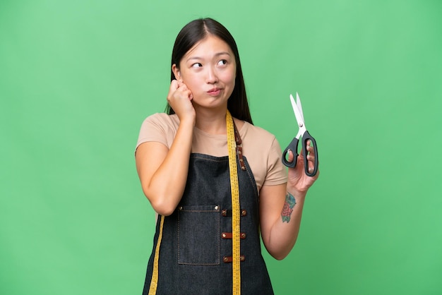 Junge asiatische Näherin über isoliertem Hintergrund frustriert und bedeckt die Ohren