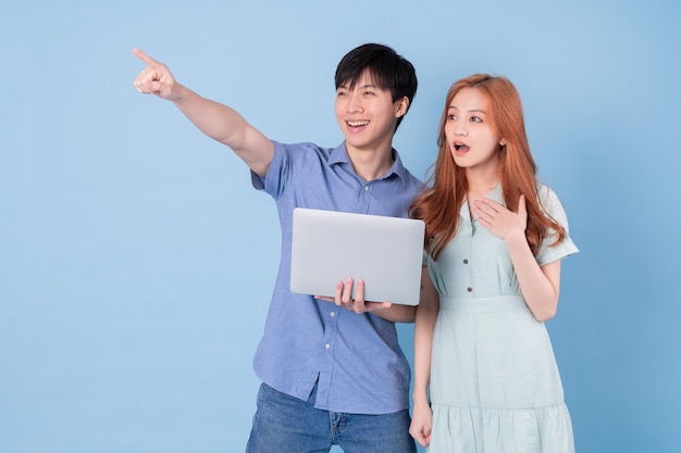 Junge asiatische Paare, die Laptop auf blauem Hintergrund verwenden