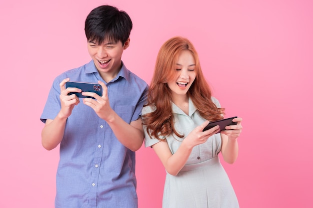 Junge asiatische Paare, die Smartphone auf rosa Hintergrund verwenden