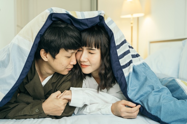 junge asiatische Paare, die zusammen unter der Decke lächeln