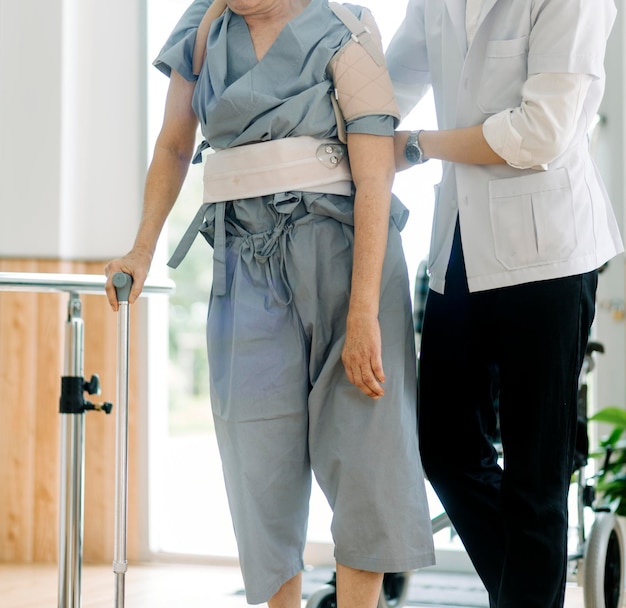 Junge asiatische Physiotherapeutin arbeitet mit altem Mann an der Arbeit mit einem Rollator im Flur des Pflegeheims