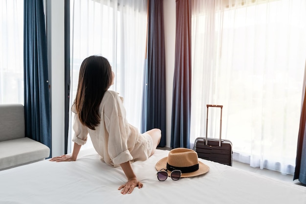 Foto junge asiatische reisende mit gepäck, die auf dem bett im hotelzimmer sitzt und sich entspannt