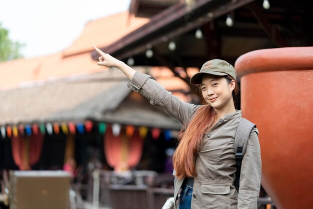 Junge asiatische reisende mit maske und rucksack, die mit dem finger auf berühmte touristenattraktionen in thailand zeigt