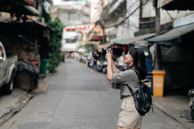 Junge asiatische Rucksackreisende mit digitaler Kompaktkamera, die den lokalen Ort und das Lächeln der Straßenkultur genießt