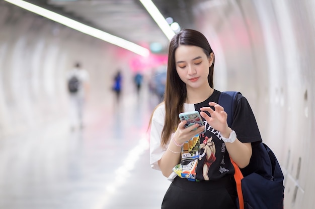 Junge asiatische schöne Frau steht im U-Bahn-Tunnel-Lifestyle, während sie Smartphone in der Hand hält