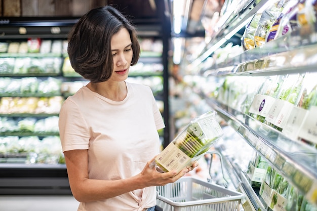 Junge asiatische Schönheit, die den Einkaufskorb geht in den Supermarkt, Kasten Salat halten hält.