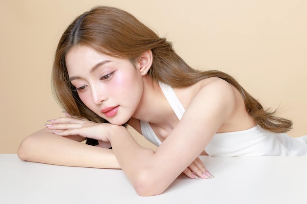 Junge asiatische Schönheit Frau lockiges langes Haar mit koreanischem Make-up-Stil berühren ihr Gesicht und perfekte Haut auf isolierter beige Hintergrund Gesichtsbehandlung Kosmetologie plastische Chirurgie