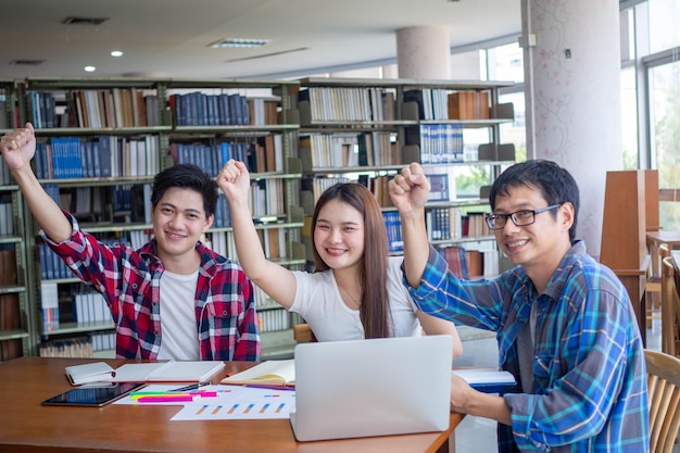 Junge asiatische Studentengruppe mit strahlendem Lächeln in der Bibliothek Die Studenten freuen sich, Informationen zu finden und über Computer zu lernen