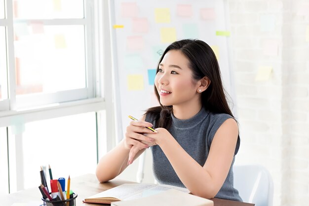 Junge asiatische Studentin, die am Tisch denkt